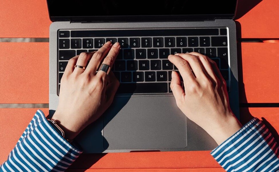 Nahaufnahme von Händen, die auf einer Laptop-Tastatur tippen, das Gerät steht auf einem roten Tisch.